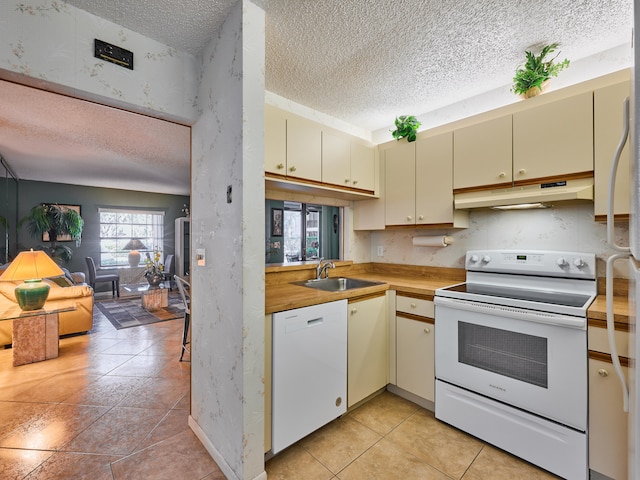 kitchen with cream cabinets, light tile patterned floors, a textured ceiling, sink, and white appliances