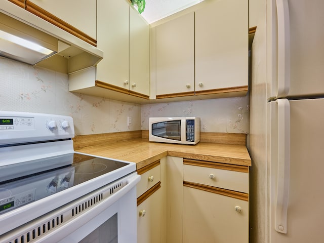 kitchen featuring butcher block counters, cream cabinets, and white appliances