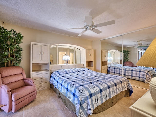 bedroom featuring a textured ceiling, light tile patterned flooring, ceiling fan, and a closet