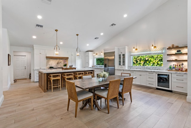 dining space with sink, high vaulted ceiling, light hardwood / wood-style floors, and beverage cooler