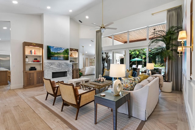 living room with ceiling fan, high vaulted ceiling, a premium fireplace, and light hardwood / wood-style floors