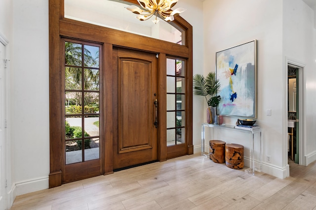 foyer entrance with a high ceiling, light wood-type flooring, and an inviting chandelier