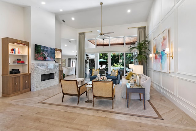 living room featuring a premium fireplace, high vaulted ceiling, light wood-type flooring, and ceiling fan