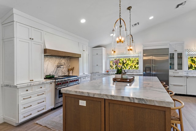 kitchen featuring a large island, premium appliances, vaulted ceiling, and white cabinets