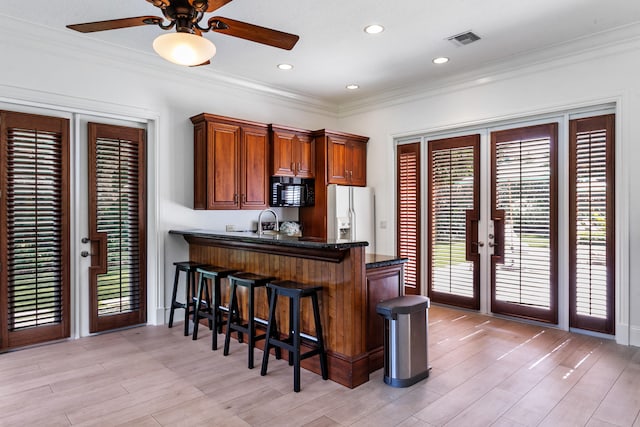 kitchen with white fridge with ice dispenser, kitchen peninsula, a kitchen breakfast bar, ceiling fan, and crown molding