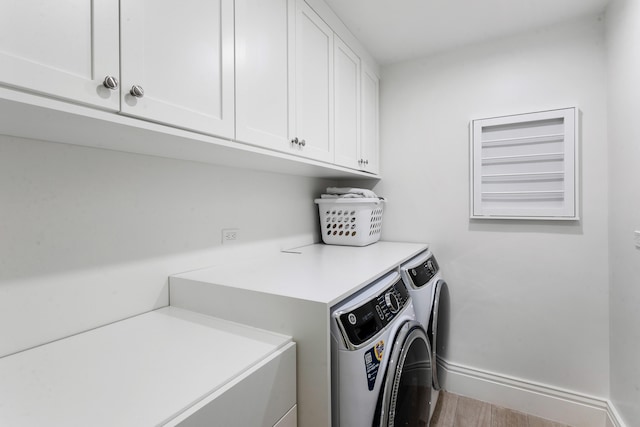 laundry room featuring washer and clothes dryer, light wood-type flooring, and cabinets