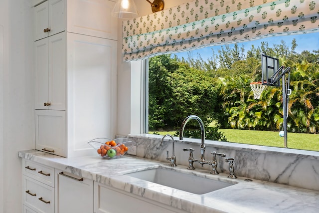 kitchen with sink, light stone countertops, white cabinets, and plenty of natural light