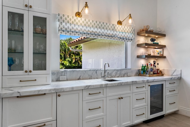 kitchen with light hardwood / wood-style flooring, sink, beverage cooler, white cabinets, and light stone counters