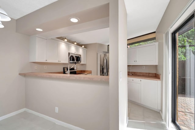 kitchen with appliances with stainless steel finishes, white cabinets, kitchen peninsula, and light tile patterned flooring