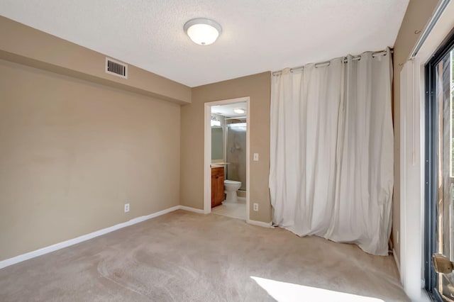 unfurnished bedroom with ensuite bath, a textured ceiling, and light colored carpet