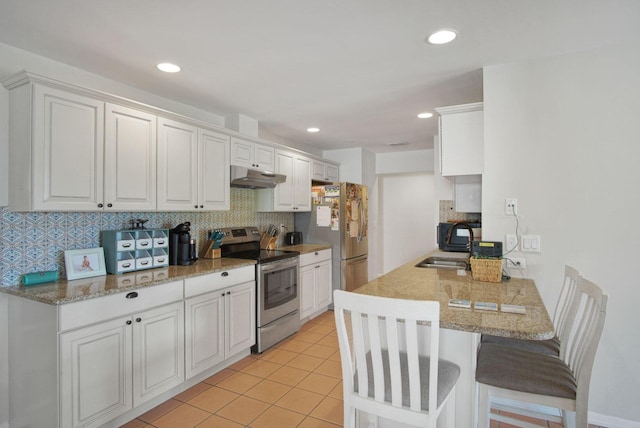 kitchen featuring tasteful backsplash, under cabinet range hood, a kitchen bar, white cabinets, and appliances with stainless steel finishes