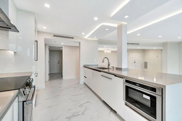 kitchen with stainless steel appliances, wall chimney range hood, white cabinetry, and sink