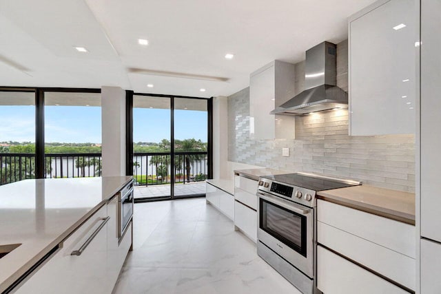 kitchen featuring white cabinetry, a water view, appliances with stainless steel finishes, backsplash, and wall chimney range hood