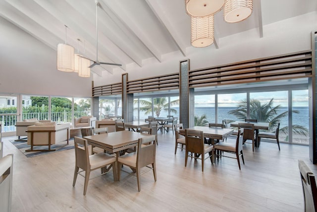 dining room with high vaulted ceiling, a water view, light hardwood / wood-style floors, and plenty of natural light