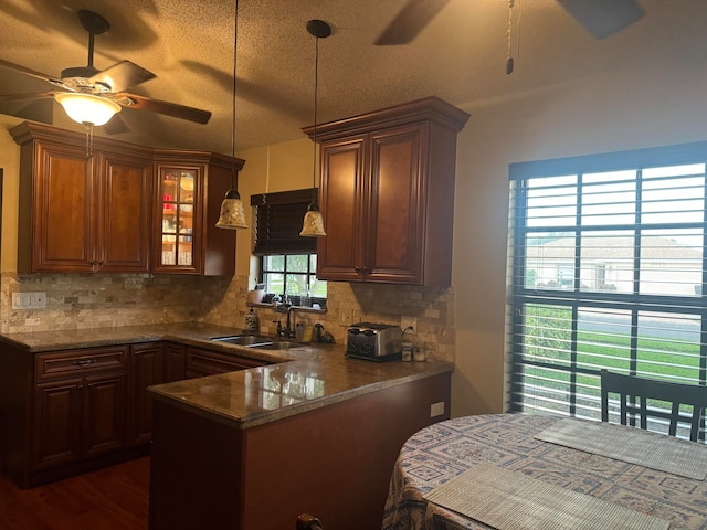 kitchen featuring kitchen peninsula, pendant lighting, backsplash, and sink