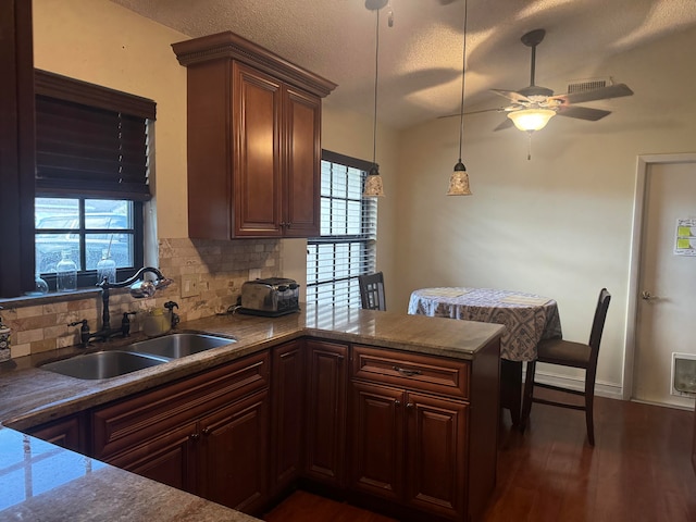 kitchen featuring backsplash, sink, dark hardwood / wood-style floors, decorative light fixtures, and kitchen peninsula