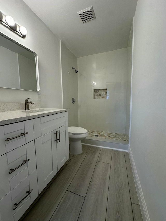 bathroom featuring vanity, a tile shower, and toilet