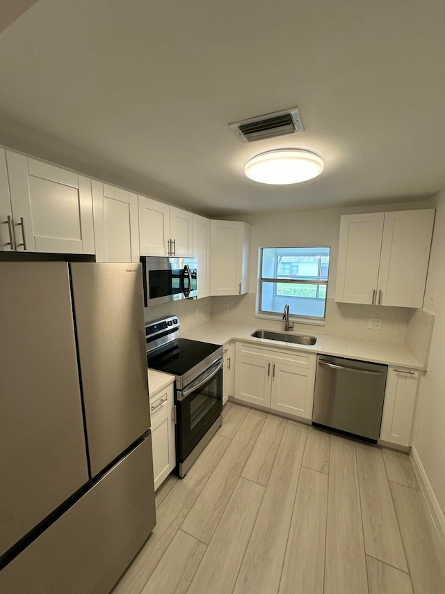 kitchen featuring sink, appliances with stainless steel finishes, light hardwood / wood-style flooring, and white cabinets