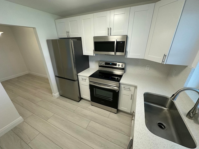 kitchen with stainless steel appliances, sink, light stone countertops, white cabinets, and light hardwood / wood-style floors