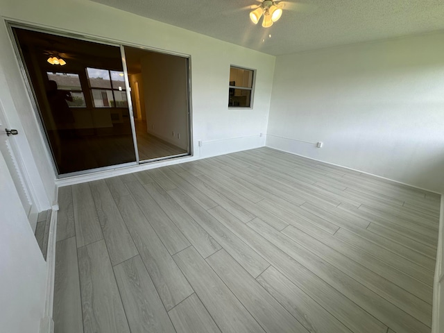 unfurnished room with ceiling fan, a textured ceiling, and light wood-type flooring