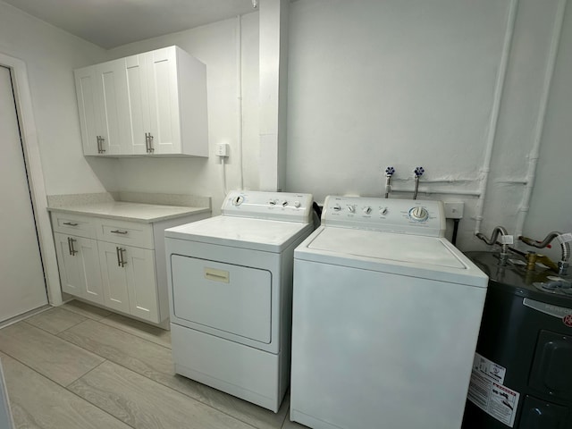 laundry room with electric water heater, independent washer and dryer, and cabinets