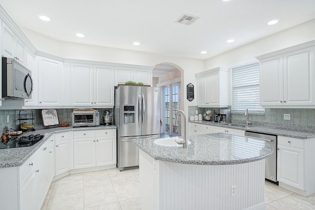 kitchen featuring appliances with stainless steel finishes, a kitchen island with sink, white cabinets, and tasteful backsplash