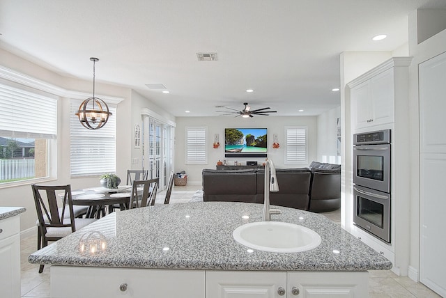 kitchen with a kitchen island with sink, sink, light tile patterned flooring, white cabinetry, and light stone counters