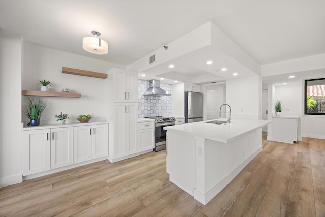 kitchen featuring appliances with stainless steel finishes, sink, wall chimney range hood, a center island with sink, and white cabinets