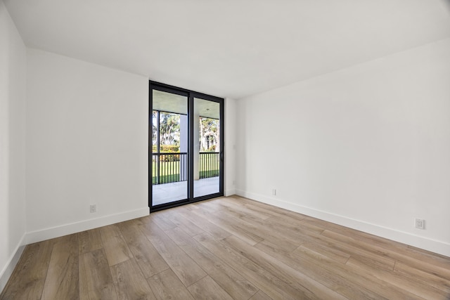 empty room with a wall of windows, wood finished floors, and baseboards