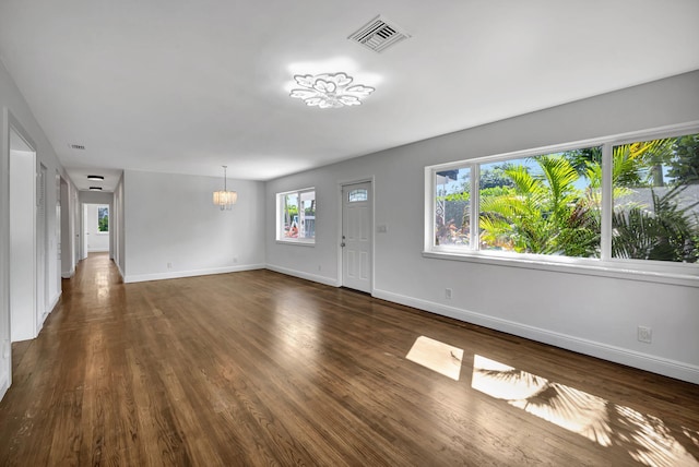 unfurnished living room with an inviting chandelier and dark wood-type flooring