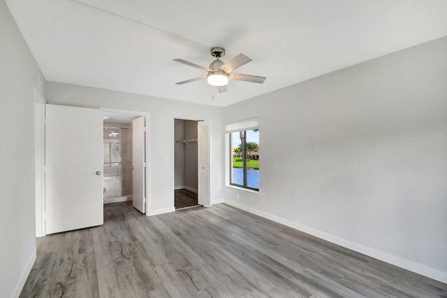 unfurnished bedroom featuring connected bathroom, a closet, a spacious closet, light hardwood / wood-style floors, and ceiling fan