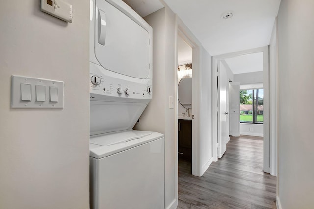 laundry area featuring stacked washer / dryer, wood-type flooring, and sink