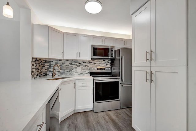 kitchen with backsplash, sink, pendant lighting, appliances with stainless steel finishes, and light hardwood / wood-style floors