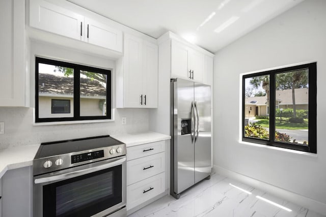 kitchen with appliances with stainless steel finishes, white cabinets, vaulted ceiling, and a wealth of natural light