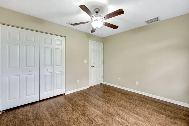 unfurnished bedroom with a textured ceiling, ceiling fan, dark hardwood / wood-style floors, and a closet