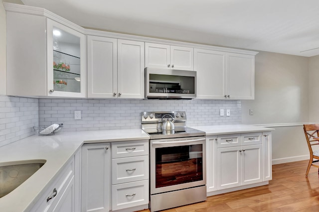 kitchen featuring white cabinets, light wood-type flooring, stainless steel appliances, and tasteful backsplash