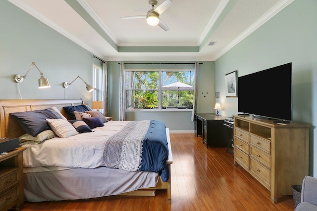 bedroom featuring ceiling fan, a raised ceiling, ornamental molding, and hardwood / wood-style floors