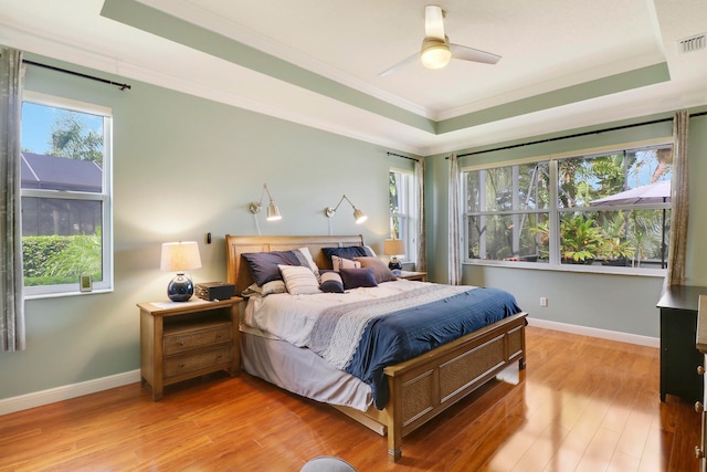 bedroom with ornamental molding, wood-type flooring, a raised ceiling, and ceiling fan