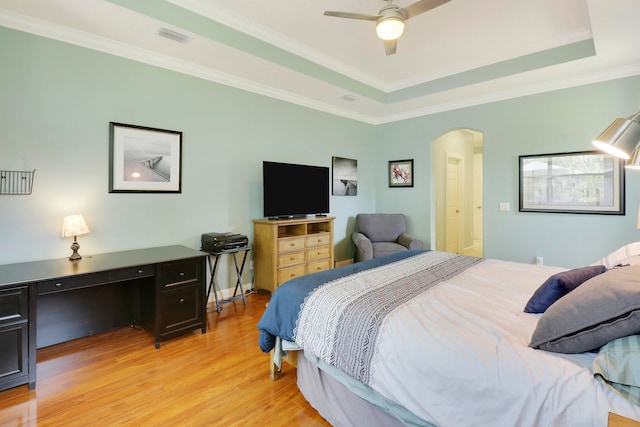 bedroom with crown molding, a tray ceiling, light hardwood / wood-style floors, and ceiling fan