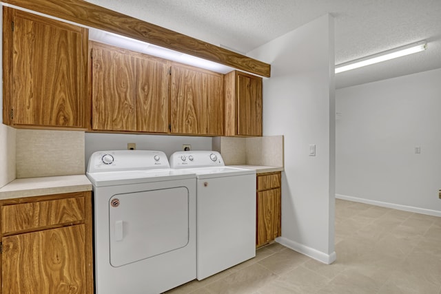 clothes washing area with independent washer and dryer, cabinets, and a textured ceiling