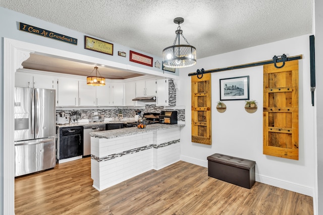 kitchen with kitchen peninsula, a barn door, white cabinetry, appliances with stainless steel finishes, and decorative light fixtures