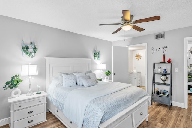 bedroom featuring a textured ceiling, light hardwood / wood-style flooring, ceiling fan, and connected bathroom