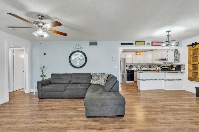 living room with light wood-type flooring, a barn door, ceiling fan, and a textured ceiling