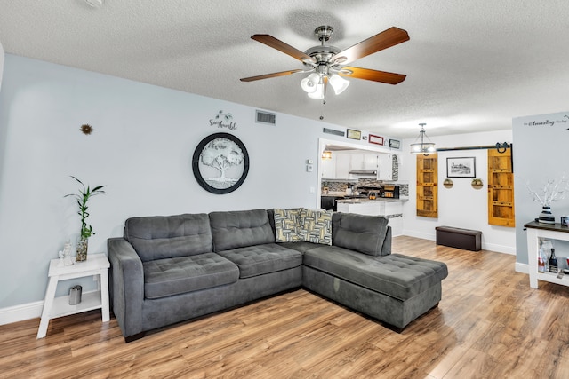 living room with a textured ceiling, light wood-type flooring, and ceiling fan