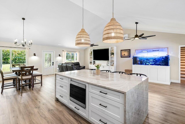 kitchen with white cabinetry, vaulted ceiling, stainless steel microwave, and light wood-type flooring