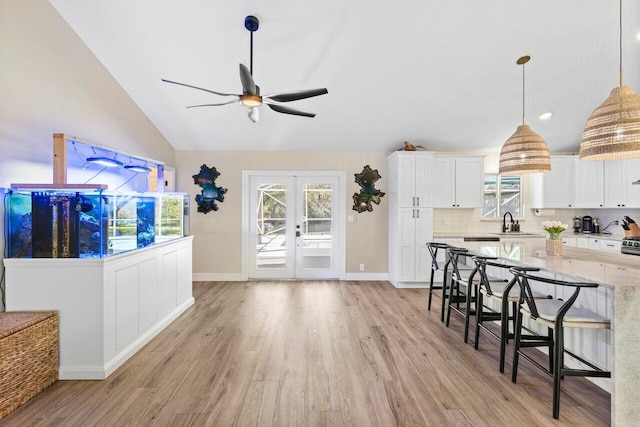 kitchen with a breakfast bar area, light hardwood / wood-style flooring, decorative light fixtures, white cabinetry, and light stone counters