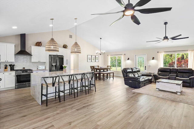 kitchen featuring wall chimney range hood, white cabinets, a breakfast bar, pendant lighting, and stainless steel appliances