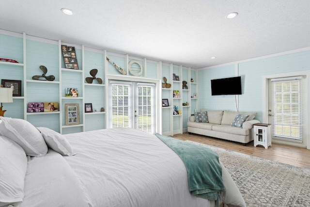 bedroom with a textured ceiling, light hardwood / wood-style flooring, multiple windows, and wood walls