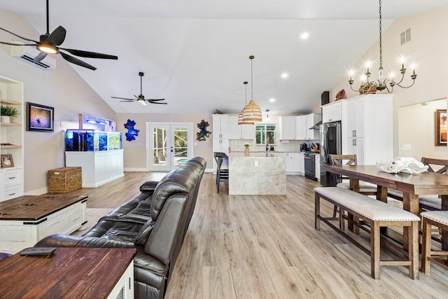 living room with ceiling fan with notable chandelier, french doors, an AC wall unit, light hardwood / wood-style floors, and high vaulted ceiling