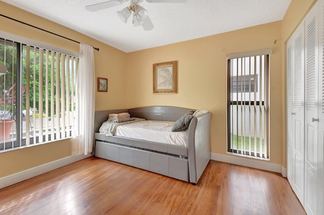 bedroom featuring light hardwood / wood-style floors, ceiling fan, multiple windows, and a closet